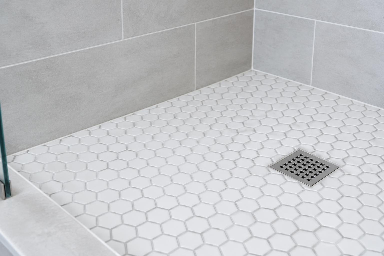 Illustrative hexagonal shower floor with uniform grout joints and a metal drain